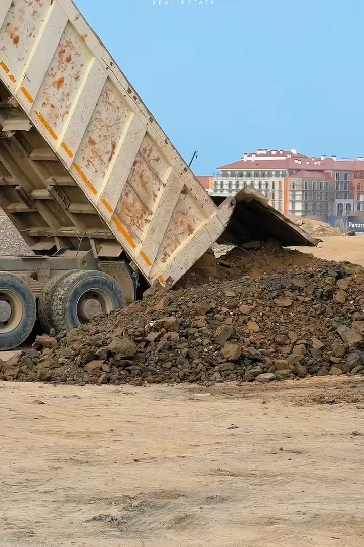 Самосвал ссыпает грунт, за ним — корпуса курорта, 15.09.2025